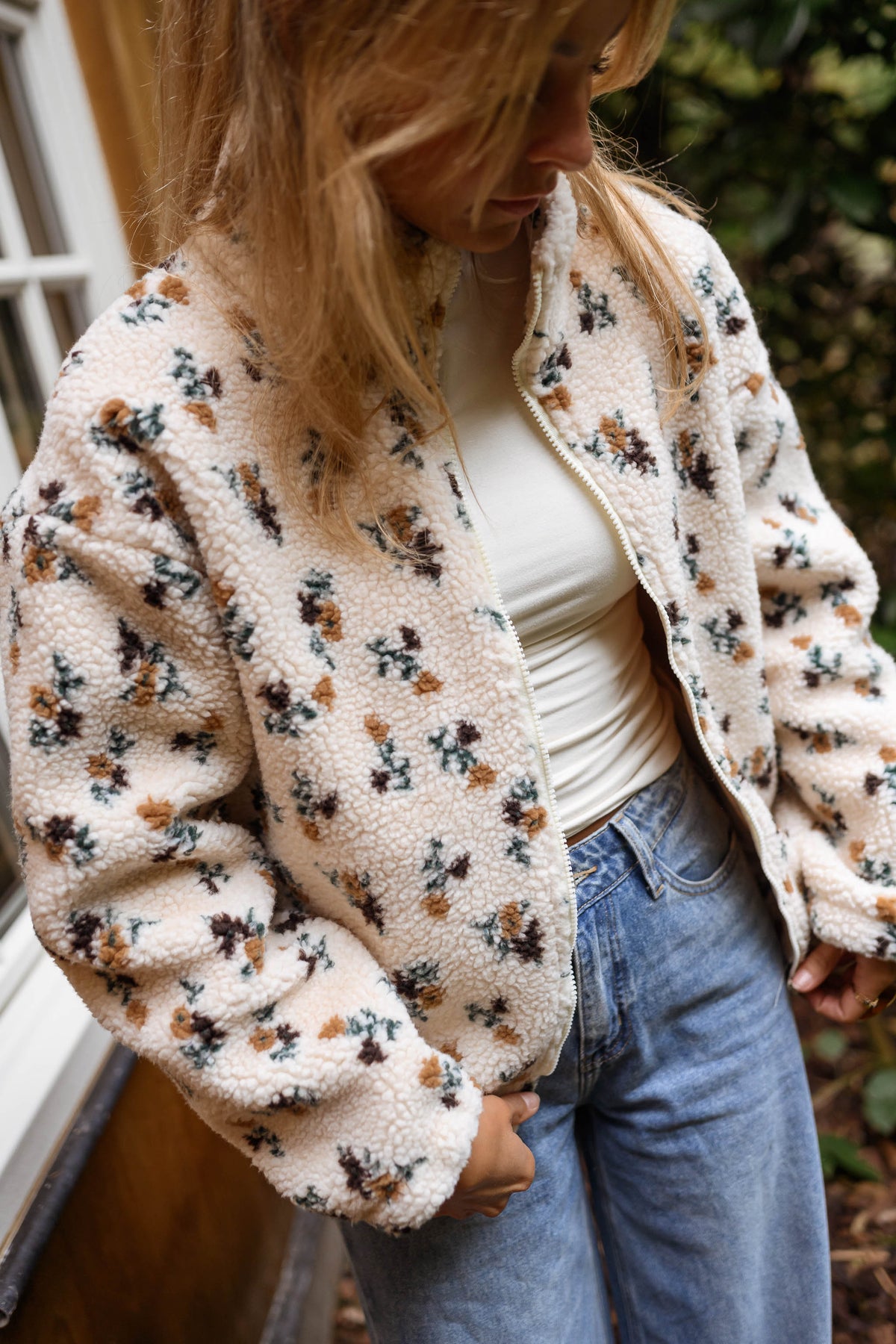 Veste polaire fleurie zippée écru portée par une femme, vue rapprochée, fleurs sombres, jean bleu