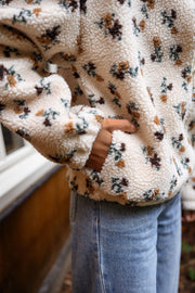 Veste polaire fleurie zippée écru portée par une femme, vue rapprochée, motif fleuri, main dans la poche