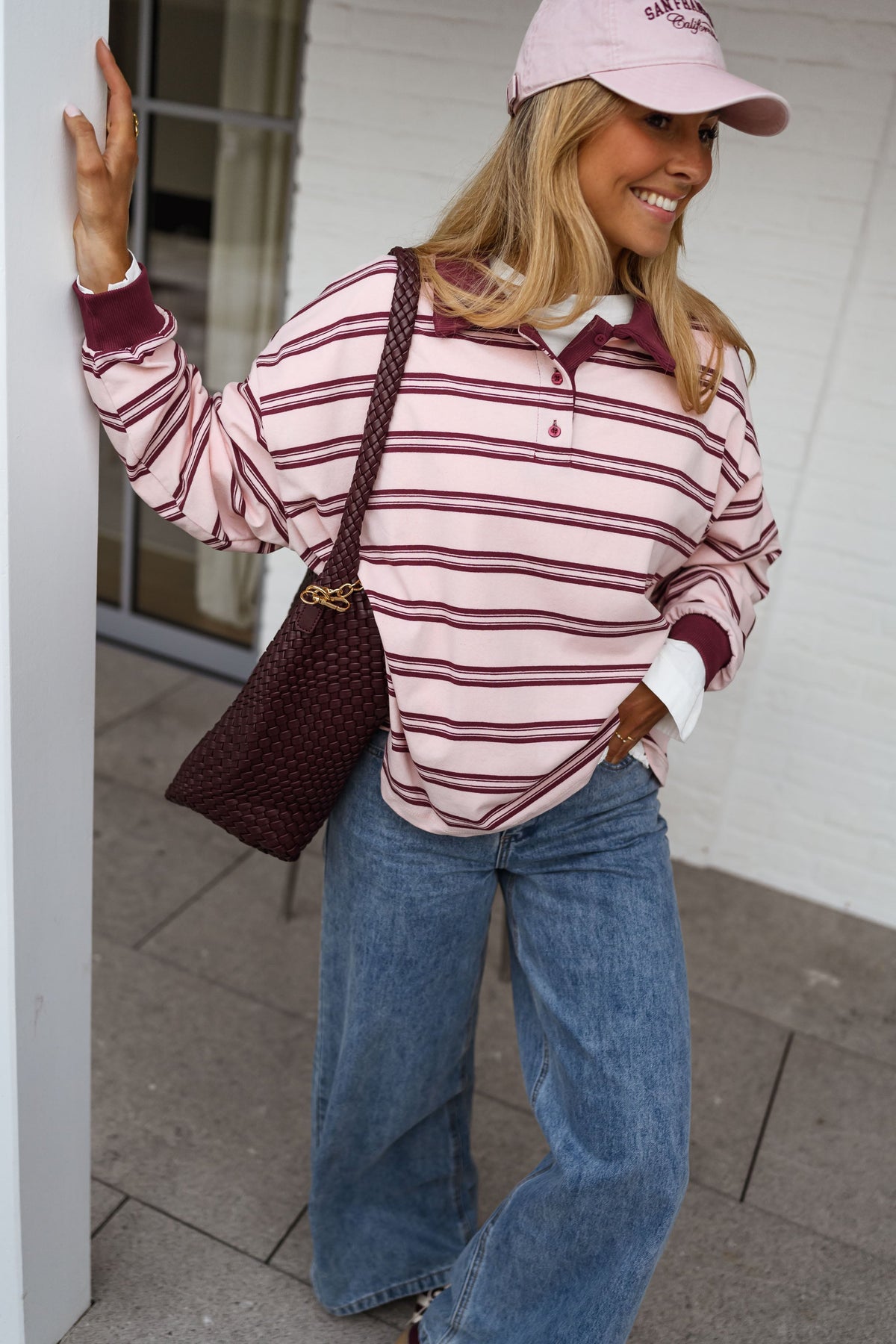 Polo loose à col revers porté par une femme, vue de face, casquette rose, sac bordeaux