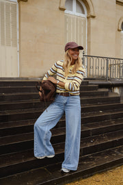 Polo rayé manches longues porté par une femme, vue de face, escalier, casquette