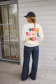 Pull doux et chaud porté par une femme, vue de dos, lettres colorées, casquette marine