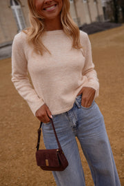 Pull dos ouvert détails dorés porté par une femme, vue de face, sac bordeaux, main dans la poche