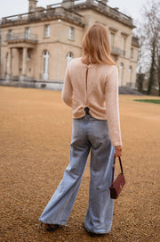 Pull dos ouvert détails dorés porté par une femme, vue de dos, esplanade, sac bordeaux