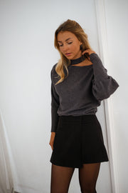 Pull à épaule dénudée gris porté par une femme, vue de trois-quarts, mur blanc, sourire
