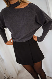 Pull à épaule dénudée gris porté par une femme, vue rapprochée, jupe noire plissée, pull gris