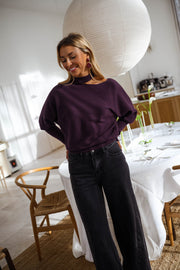 Pull à épaule dénudée prune porté par une femme, vue de face, table ronde, jean noir