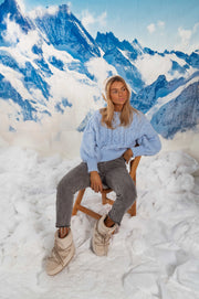 Pull torsadé légèrement loose porté par une femme, assise, chaise pliante, baskets