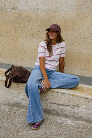 Pull en maille légère porté par une femme, assise, sur un muret, casquette, sac marron
