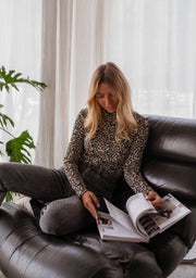 Pull léopard à col montant porté par une femme, assise, canapé noir, magazine