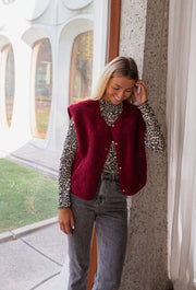 Pull léopard à col montant porté par une femme, vue de face, gilet bordeaux par-dessus, baie vitrée