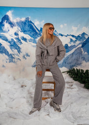 Pull doux à lien noué gris porté par une femme, vue de trois-quarts, chaise pliante, lunettes de soleil