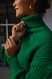 Pull vert côtelé col roulé porté par une femme, vue rapprochée, col roulé côtelé vert, boucle d'oreille