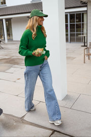 Pull vert côtelé col roulé porté par une femme, vue de face, casquette verte, mains jointes