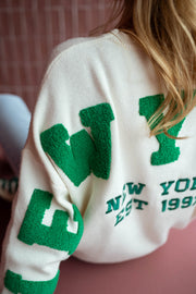 Pull loose à logo dos écru porté par une femme, vue rapprochée, lettres vertes, inscription