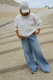 Pull ample à inscriptions porté par une femme, silhouette entière, casquette grise, mains dans les poches