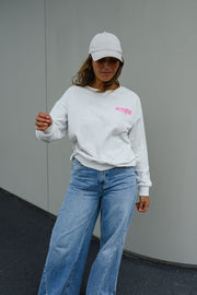 Pull ample à inscriptions porté par une femme, vue de trois-quarts, casquette grise, devant un mur gris