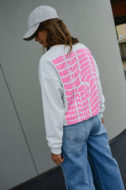 Pull ample à inscriptions porté par une femme, vue de dos, motif rose dans le dos, casquette