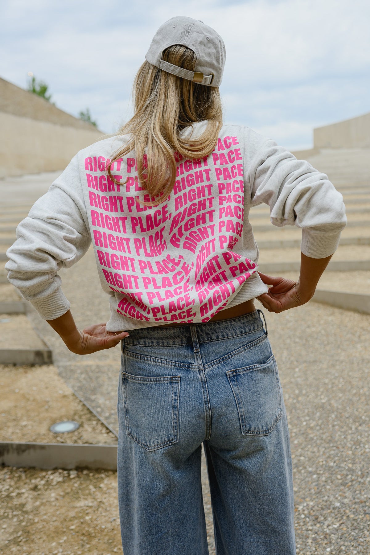 Pull ample à inscriptions porté par une femme, vue de dos, motif rose dans le dos, mains sur les hanches