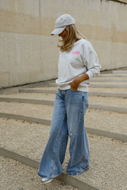 Pull ample à inscriptions porté par une femme, silhouette entière, casquette grise, sur des gradins