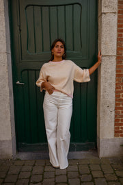 Pull loose à manches courtes porté par une femme, vue de trois-quarts, pantalon blanc, devant une porte verte