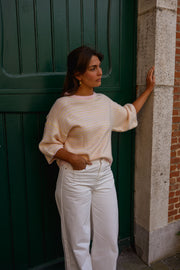 Pull loose à manches courtes porté par une femme, silhouette entière, pantalon blanc, devant une porte verte