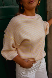 Pull loose à manches courtes porté par une femme, vue rapprochée, main sur le ventre, pantalon blanc