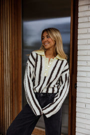 Pull rayé à manches évasées porté par une femme, vue de trois-quarts, porte en bois, sourire