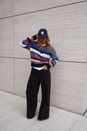 Pull rayé à col rond porté par une femme, vue de face, casquette marine, mains dans les poches