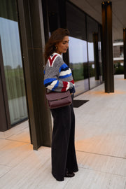 Pull rayé à col rond porté par une femme, vue de trois-quarts, sac bordeaux, baie vitrée