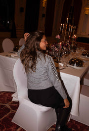 Pull à manches pailletées gris porté par une femme, vue de dos, dos, chaise blanche