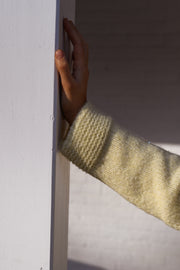 Pull col rond légèrement ample porté par une femme, vue rapprochée, manche, main contre le mur