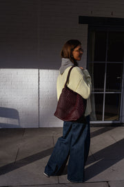 Pull col rond légèrement ample porté par une femme, vue de trois-quarts, sac bordeaux, mur blanc
