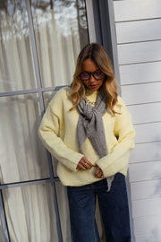 Pull col rond légèrement ample porté par une femme, vue de face, foulard gris, rideaux blancs