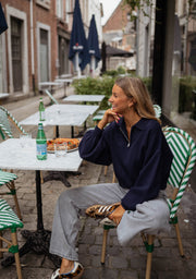 Pull court à col zippé bleu porté par une femme, assise, terrasse, jambes croisées