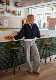 Pull court à col zippé bleu porté par une femme, silhouette entière, bar, tabourets