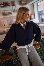 Pull court à col zippé bleu porté par une femme, vue de face, tabourets, jean gris