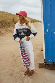 Pull loose à col polo porté par une femme, silhouette entière, casquette rouge, serviette à la main