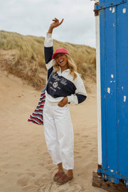 Pull loose à col polo porté par une femme, silhouette entière, bras levé, cabine bleue