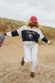 Pull loose à col polo porté par une femme, silhouette entière, bras écartés, sur la plage