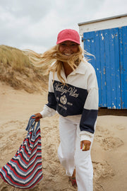 Pull loose à col polo porté par une femme, en marchant, casquette rouge, serviette à la main
