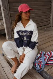 Pull loose à col polo porté par une femme, assise, sur un banc, casquette rouge, vue de face