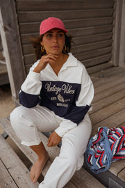 Pull loose à col polo porté par une femme, assise, casquette rouge, sur un banc