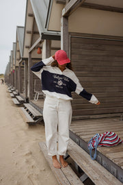 Pull loose à col polo porté par une femme, silhouette entière, bras écartés, devant des cabines