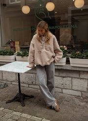Pull ample à capuche zippé beige porté par une femme, silhouette entière, table, vitrine