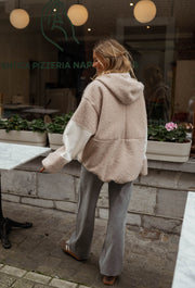 Pull ample à capuche zippé beige porté par une femme, vue de dos, capuche, table