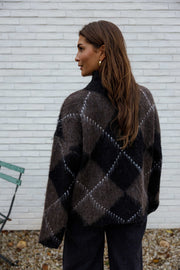 Pull jacquard col montant porté par une femme, vue de dos, mur blanc, cheveux bruns