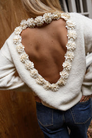 Pull à dos ouvert fleuri écru porté par une femme, vue rapprochée, fleurs en relief, dos nu