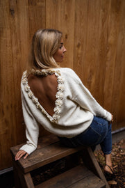 Pull à dos ouvert fleuri écru porté par une femme, vue de dos, tabouret en bois, fleurs