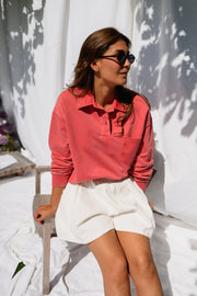 Pull délavé col boutonné porté par une femme, assise, sur une chaise, jupe blanche