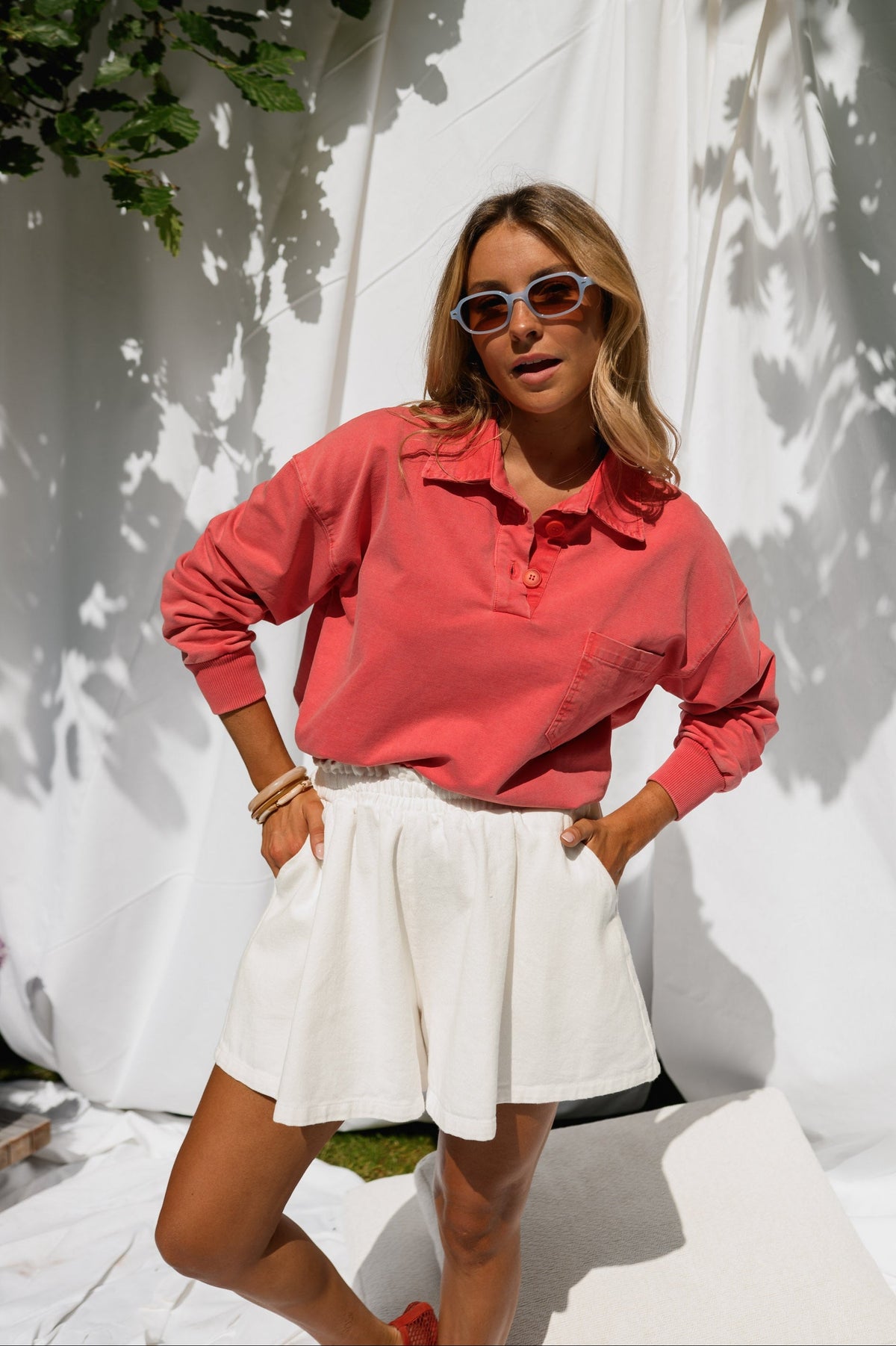 Pull délavé col boutonné porté par une femme, silhouette entière, jupe blanche, lunettes de soleil